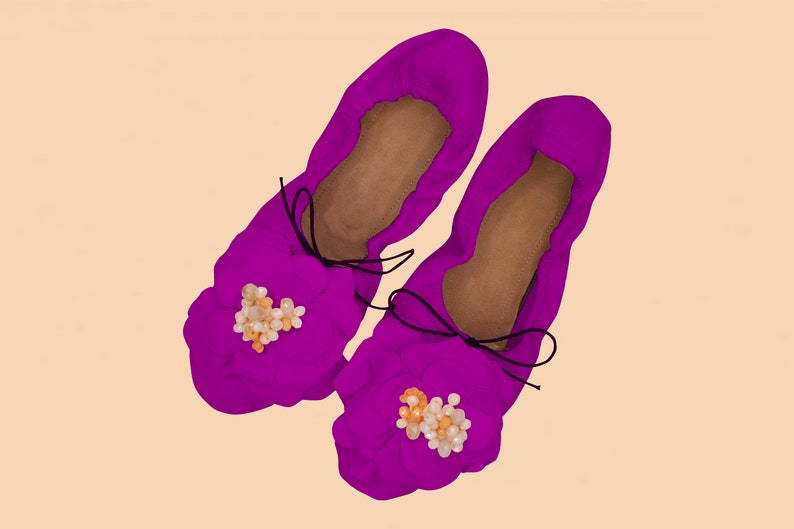 May include: A pair of purple fabric ballet flats with a flower embellishment made of white and orange beads.
