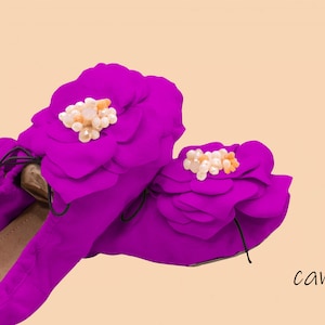 May include: A pair of magenta ballet flats with a large flower design on the top. The flowers have a cluster of small, white and orange beads in the center.