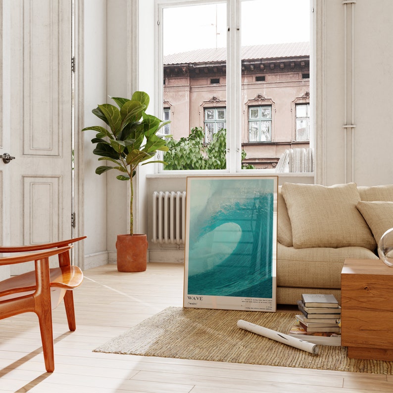 May include: A framed poster with a photograph of a large wave crashing. The poster is hanging on a white wall in a living room with a beige couch, a wooden coffee table, and a potted plant.