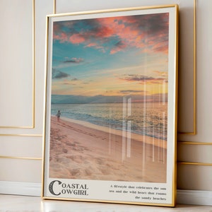 May include: A framed print with a sunset over the ocean and a person walking on the beach. The text "Coastal Cowgirl" is at the bottom of the print. The text reads "A lifestyle that celebrates the sun, sea and the wild heart that roams the sandy beaches."