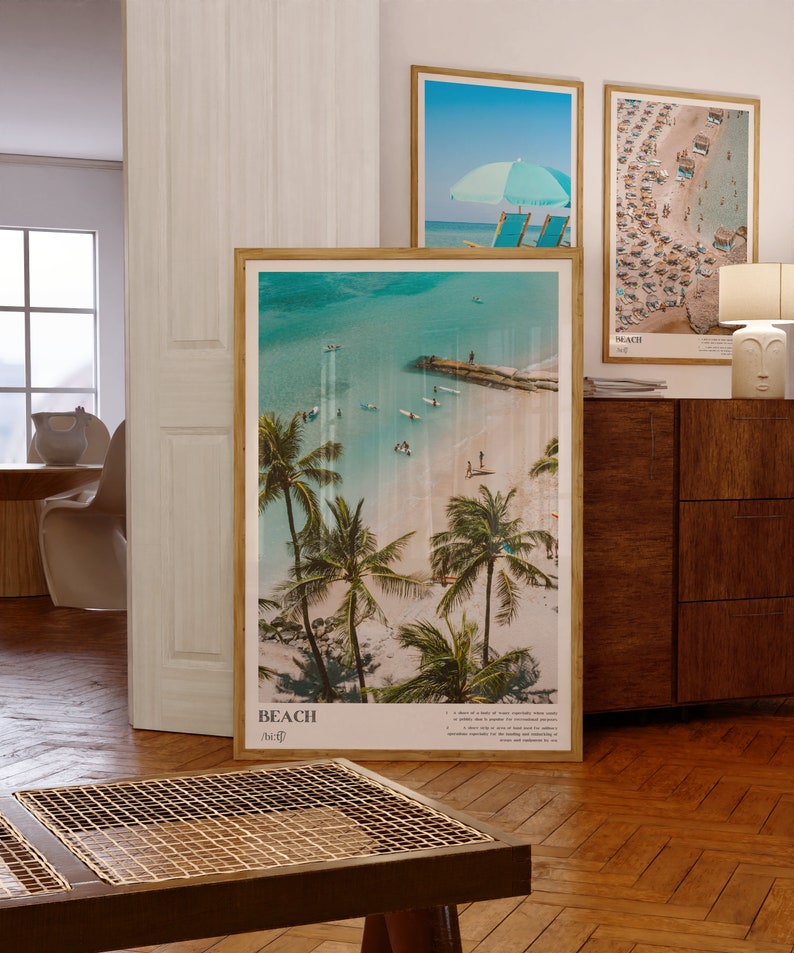 May include: Three framed beach-themed prints. The largest features a tropical beach scene with palm trees, turquoise water, and the word "BEACH". The other two prints show beach scenes with umbrellas and beachgoers. All are in wooden frames.