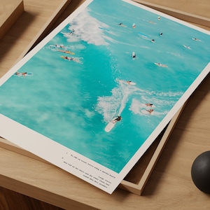 May include: An aerial view of surfers riding waves on a bright turquoise ocean. The surfers are riding on longboards and shortboards, and the waves are breaking in the distance.