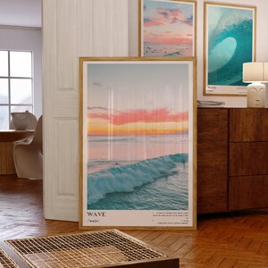 May include: Three framed prints of ocean waves. The top left print shows a pink and orange sunset over the ocean. The top right print shows a large blue wave breaking. The bottom print shows a wave breaking at sunset with surfers in the water. The prints have the word "WAVE" and the phonetic spelling "/weɪv/" printed below the image.