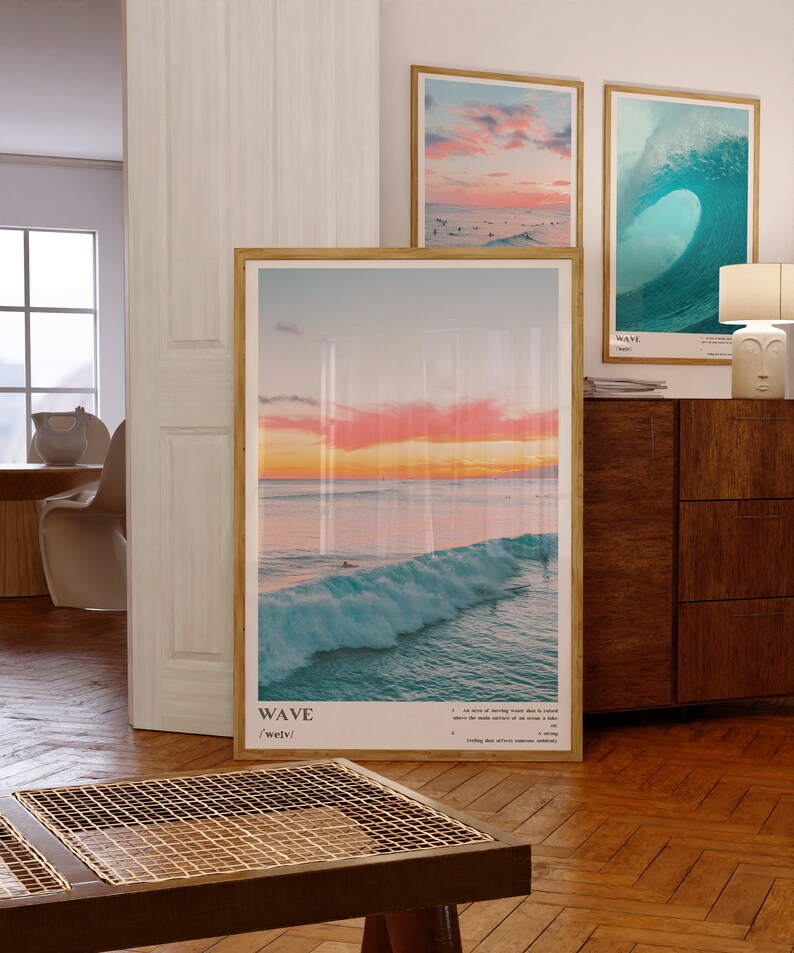 May include: Three framed prints of ocean waves. The top left print shows a pink and orange sunset over the ocean. The top right print shows a large blue wave breaking. The bottom print shows a wave breaking at sunset with surfers in the water. The prints have the word "WAVE" and the phonetic spelling "/weɪv/" printed below the image.