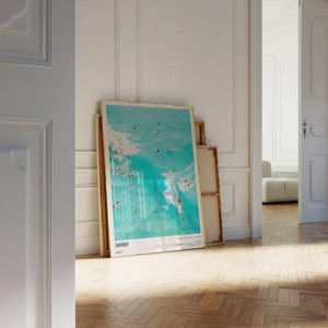 May include: A framed poster with a blue and white image of surfers riding waves. The poster has the word "SURF" printed in black at the bottom.