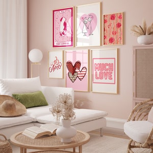 May include: A living room interior with a white sectional sofa, a coffee table, and a wicker chair. The walls are painted a light pink color and decorated with six framed prints featuring hearts, flowers, and the words "Te Amo", "Much Love", and "The Lovers".