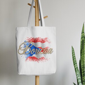 Puede incluir: Bolsa de tela blanca con un dise&ntilde;o de bandera puertorrique&ntilde;a roja, blanca y azul y la palabra "Boruc&uacute;a" en letras doradas con brillantina.