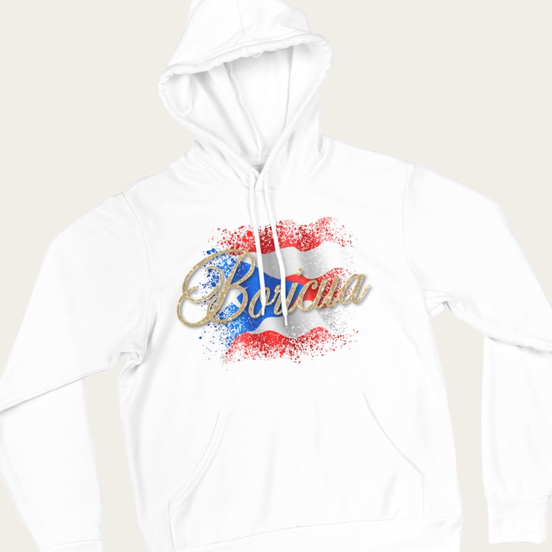 Puede incluir: Sudadera blanca con un dise&ntilde;o de la bandera puertorrique&ntilde;a en purpurina dorada y la palabra "Bor&iacute;cua" en purpurina dorada.