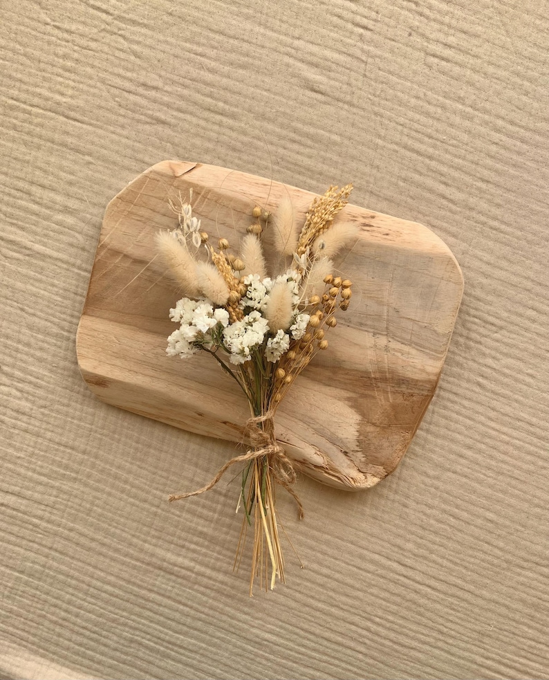 Puede incluir: Un peque&ntilde;o ramo de flores secas en tonos blancos y beige, atado con cuerda, sobre una superficie de madera.