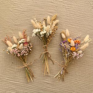 Puede incluir: Tres peque&ntilde;os ramos de flores secas atados con cuerda. Los ramos presentan una variedad de flores secas en tonos de blanco, rosa, morado, amarillo y naranja.