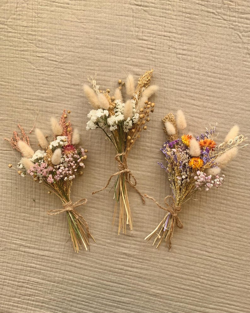 Puede incluir: Tres peque&ntilde;os ramos de flores secas atados con cuerda. Los ramos presentan una variedad de flores secas en tonos de blanco, rosa, morado, amarillo y naranja.