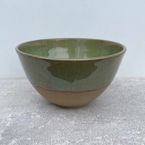 May include: A green ceramic bowl with a brown rim. The bowl is glazed and has a speckled finish.