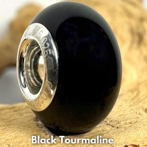 Peut inclure: Une perle ronde et lisse en tourmaline noire avec une surface polie et un noyau central en argent sterling. Le noyau en argent porte l'inscription S925, indiquant sa composition, et est visible au centre de la perle de manière très nette.