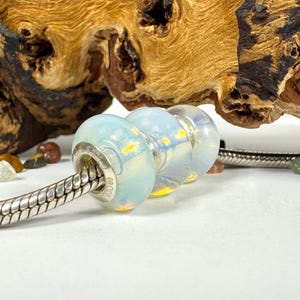 May include: Three glass beads with a milky white and iridescent finish. The beads are strung on a silver chain.