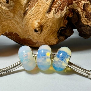 May include: Three white and blue glass beads with a silver charm bracelet. The beads have a translucent, iridescent finish.