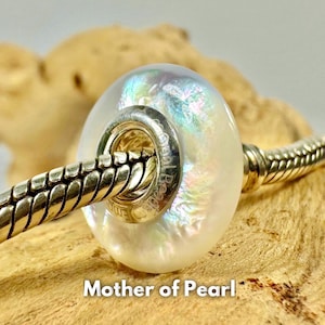 Könnte beinhalten: Eine runde, irisierende Perlmuttperle mit einem silberfarbenen Metallkern. Die Perle ist an einem silberfarbenen Armband aufgereiht. Der Text "Mother of Pearl" wird am unteren Rand des Bildes angezeigt.