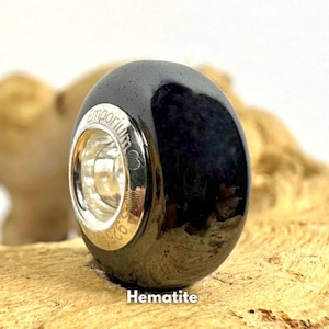 Könnte beinhalten: Eine schwarze Hämatitperle mit silbernen Akzenten. Die Perle ist mit dem Wort "Emporium" graviert.