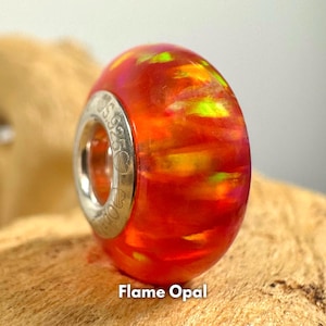 May include: A vibrant, flame opal bead with a polished, rounded shape. The bead features a fiery blend of red, orange, and yellow hues, with a silver-toned metal ring. The text "Flame Opal" is at the bottom.
