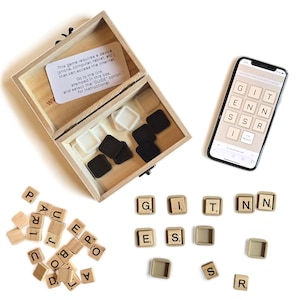 May include: A wooden box with a note inside that says "This game requires a device (phone, computer, tablet, etc.) that can access the internet. Go to the link stamped in this box, and select the "GUIDE" option for instructional." The box is open and contains black and white tiles. A smartphone with a screen displaying the words "GIT ENN SS I" is on a white surface. There are also wooden letter tiles that spell out the words "GIT ENN SS I" on the white surface.