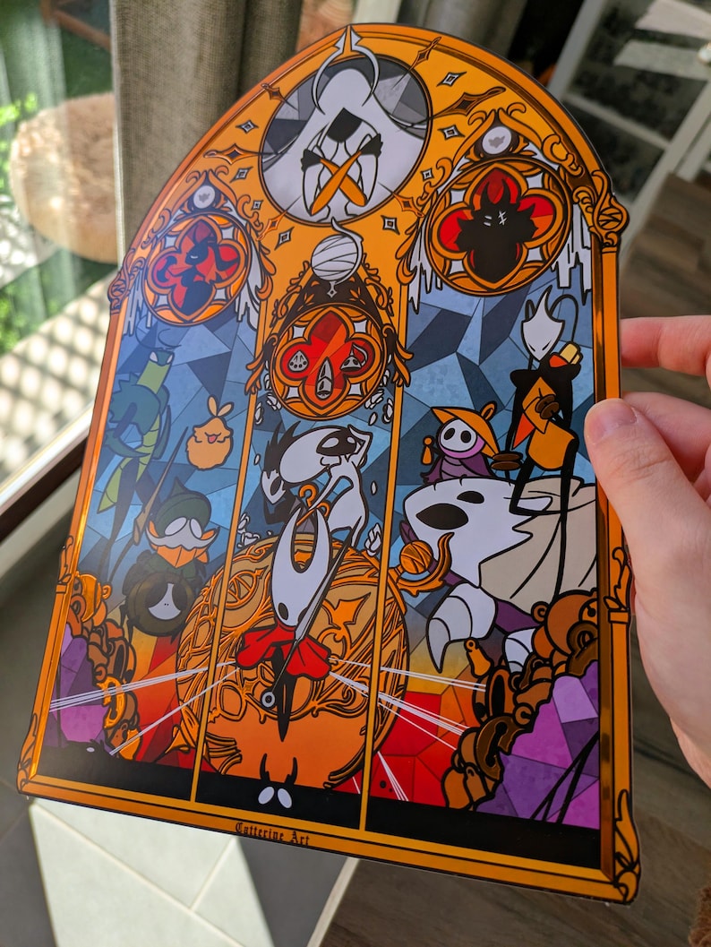 May include: A stained-glass style art print featuring characters from the video game Hollow Knight. The artwork has a gold border and depicts various characters in a colourful, geometric design. The print has the text "Cattering Art" at the bottom.