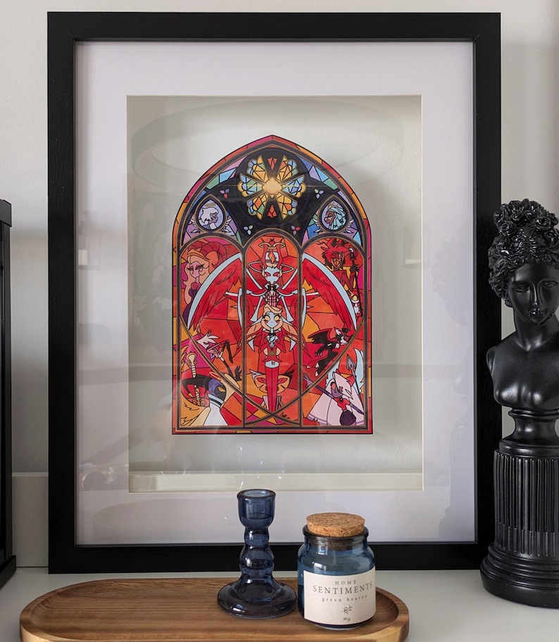 May include: A framed print of a stained glass window with a red, orange, and yellow color scheme. The window depicts a variety of figures, including a woman with wings and a crown. The text "HOME SENTIMENTS" is visible on a small jar in the foreground.