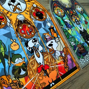 May include: Two stained glass art pieces with vibrant illustrations of video game characters. The artwork is designed to resemble stained glass windows, with orange, yellow, blue, and green colours. The text "Cutterine Art" is visible.