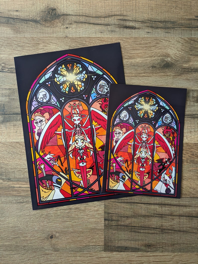 May include: Two framed prints of a stained glass window design featuring a red-haired character with wings and a halo. The design is set against a black background with a gold halo and a red, orange, and yellow stained glass pattern.