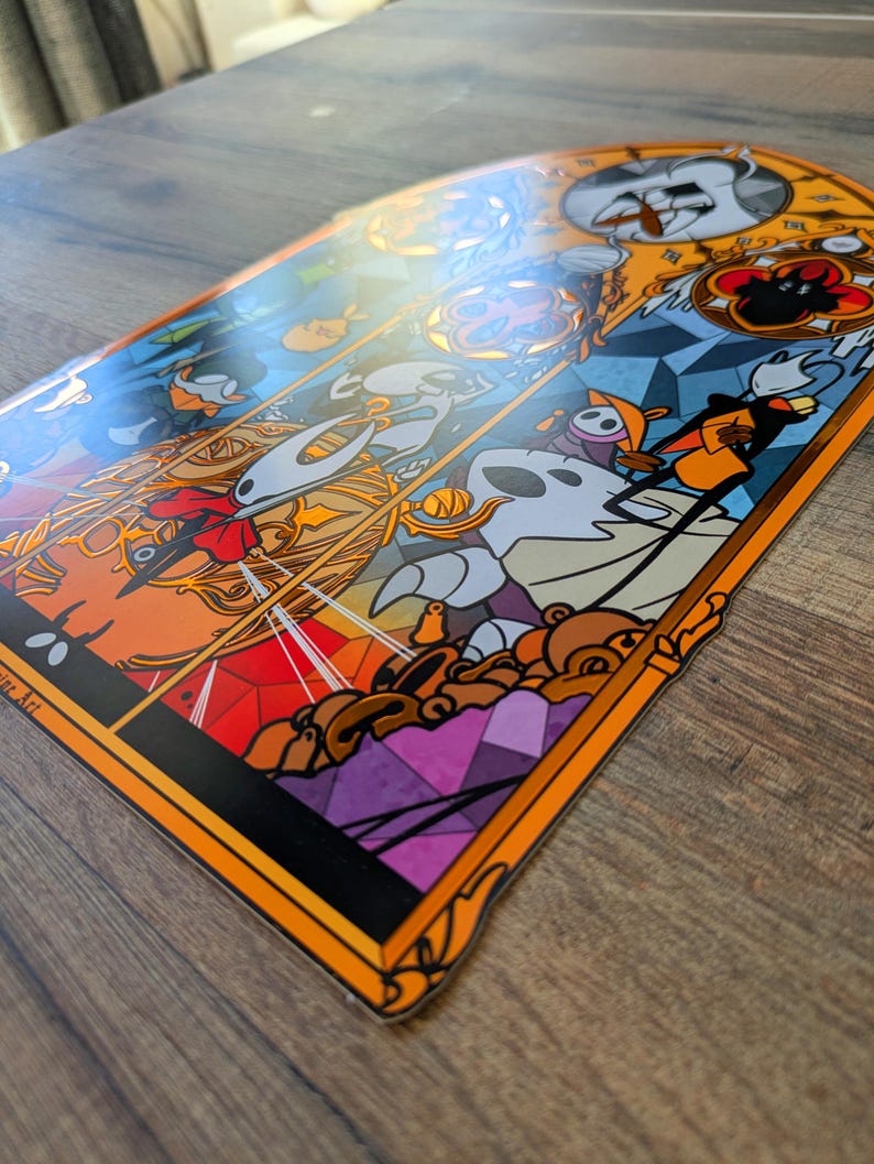 May include: A colourful sticker with a stained-glass style design, featuring cartoon characters. The sticker has an orange border and a glossy finish. The artwork includes shades of orange, blue, white, and purple, creating a vibrant and detailed image.