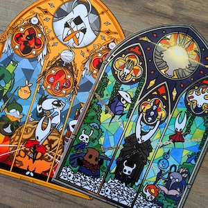 May include: Two stained-glass style art prints featuring characters from a video game. One print has an orange border, the other a blue border. Each print has a variety of characters and shapes in a stained-glass style.