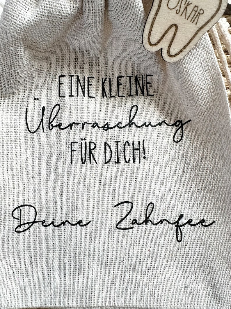 May include: A small burlap bag with a wooden tooth charm attached. The bag has the text "... Eine Kleine &Uuml;berraschung F&uuml;r Dich! Deine Zahnfee" printed on it.