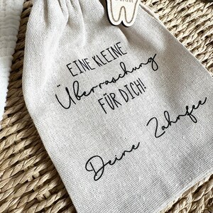 May include: A small white cloth bag with a wooden tooth-shaped tag that says "OSKAR" on it. The bag has black text that says "Eine kleine &Uuml;berraschung f&uuml;r dich! Deine Z&auml;hne".