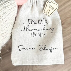 May include: A small white cloth bag with a tooth-shaped wooden tag that says "Oskar". The bag has black text that says "Eine kleine &Uuml;berraschung f&uuml;r dich! Deine Zahnfee".