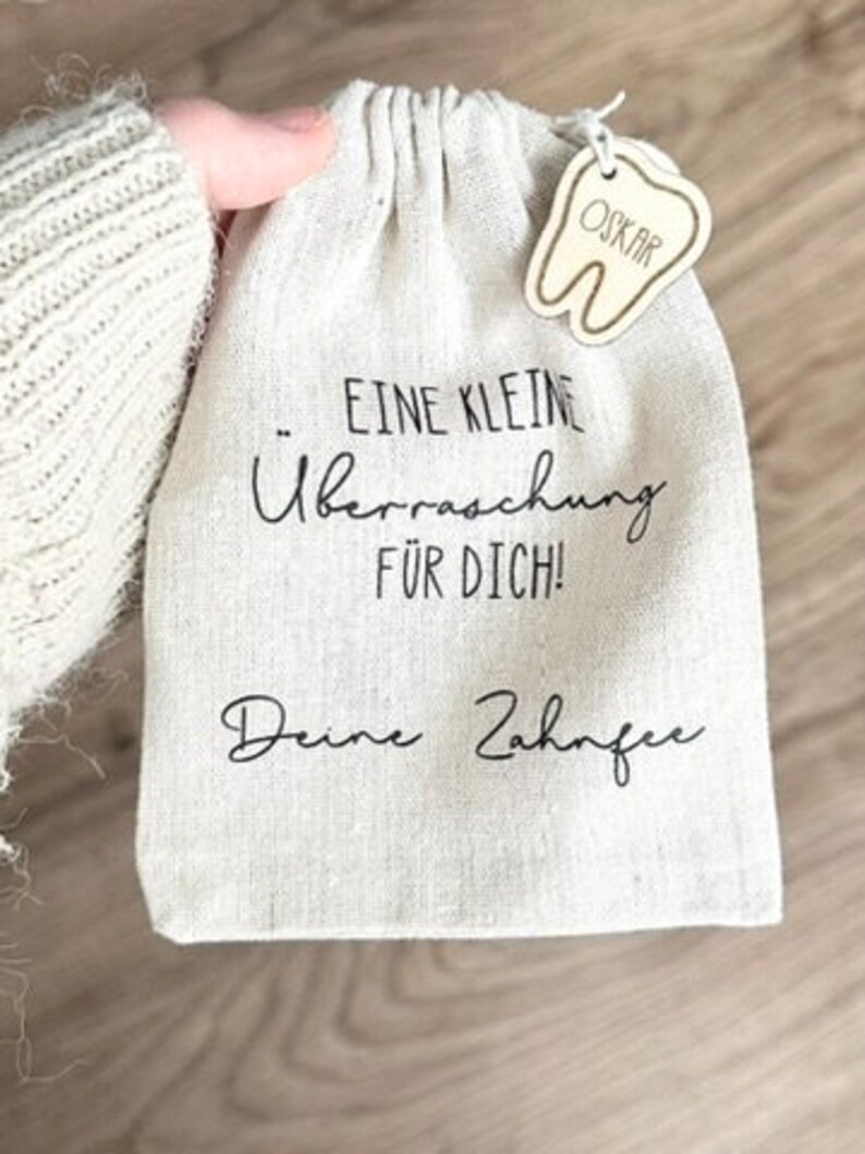 May include: A small white cloth bag with a tooth-shaped wooden tag that says "Oskar". The bag has black text that says "Eine kleine &Uuml;berraschung f&uuml;r dich! Deine Zahnfee".