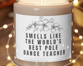 May include: A brown soy wax candle with a white label that reads "Smells like the world's best pole dance teacher". The candle is on a wooden coaster and surrounded by string lights.