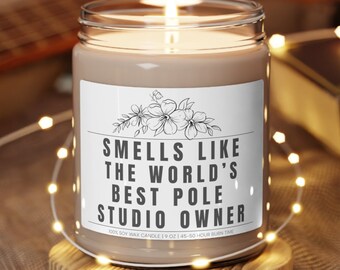May include: A brown soy wax candle with a white label that reads "Smells like the world's best pole studio owner". The candle is lit and sitting on a wooden coaster.