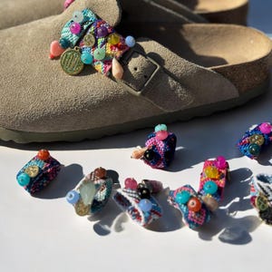 Peut inclure: Sandales en daim beige avec des lanières décoratives ornées de perles colorées. Plusieurs accessoires de lanières perlées supplémentaires sont disposés autour des sandales, avec diverses couleurs et embellissements. Semelle intérieure en liège.
