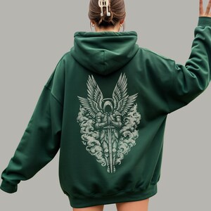 Op de afbeelding: Donkergroene hoodie met een witte afbeelding op de rug. De afbeelding is een gedetailleerde illustratie van een engel met een zwaard, omringd door wolken. De hoodie heeft een capuchon en een relaxte pasvorm.