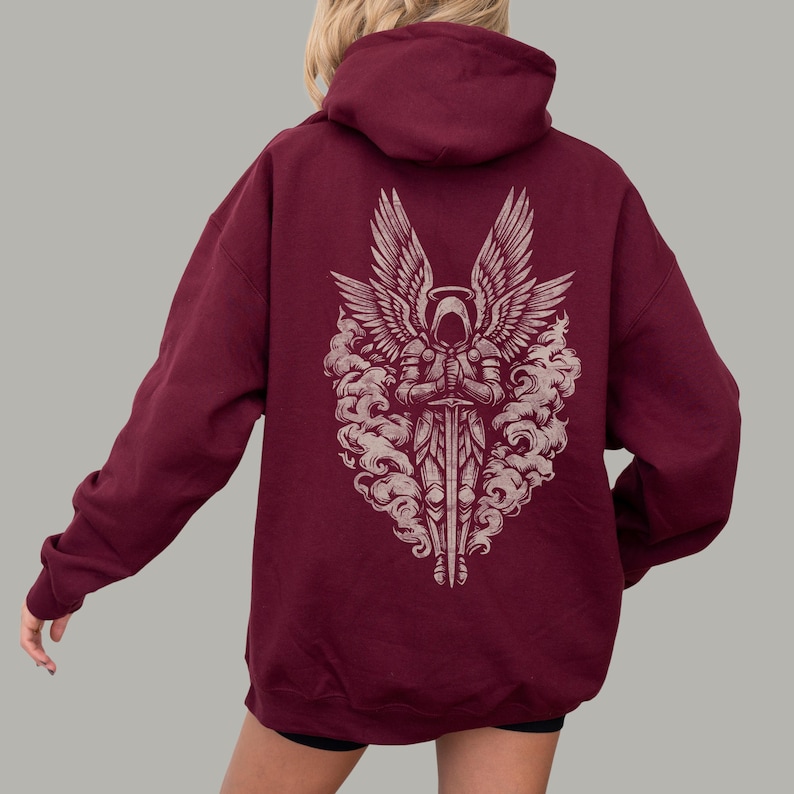 Op de afbeelding: Bordeaux hoodie met een gedetailleerde afbeelding op de rug. Het ontwerp toont een engelachtig figuur met grote vleugels, die een zwaard vasthoudt, omringd door wolkenachtige elementen. De hoodie heeft een capuchon en lange mouwen.