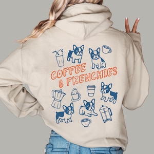 May include: A beige hooded sweatshirt featuring a back graphic with the text COFFEE & FRENCHIES in orange. The design includes blue line art illustrations of four French Bulldog dogs, a coffee press, a moka pot, and various coffee cups.