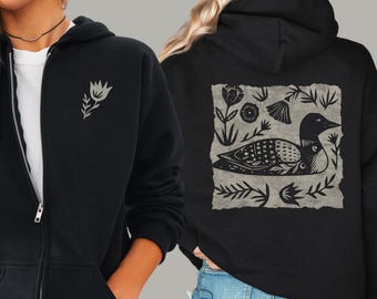 Sudadera con capucha y cremallera con estampado de pájaro estilo linograbado, inspirada en el arte popular del somormujo.