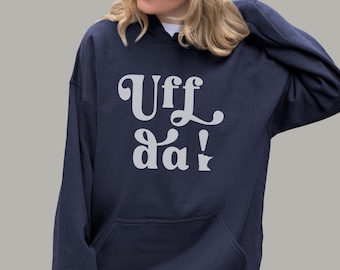 May include: Navy blue hoodie with the text "Uff da!" in a white, stylized font. The hoodie has a front pocket and a drawstring hood. The image shows a person wearing the hoodie.