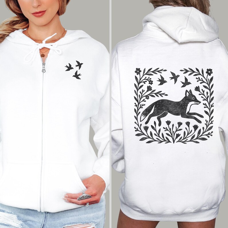 May include: A white zip-up hoodie featuring a small black graphic of three birds on the front left chest. The back displays a large black graphic of a fox running within a square frame of flowers and birds, all printed on a white hooded sweatshirt.