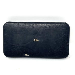 May include: A rectangular, navy blue case with rounded corners. The case has a textured surface and a small, gold-colored script logo that reads "Lilly". There is a small area of wear on the lower left side of the case.