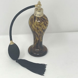 May include: An antique perfume bottle with a brown and gold spotted pattern. The bottle has a gold-colored top and a black bulb atomizer with a black tassel. The bottle is an elegant decorative item.