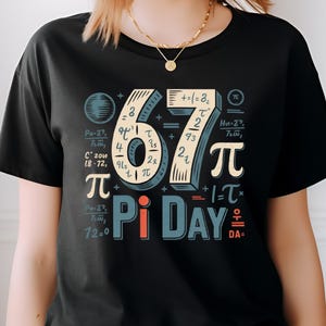 May include: Black t-shirt with a colorful graphic celebrating Pi Day. The design features the numbers "67", mathematical symbols, and the words "Pi Day". The shirt has a crew neck and short sleeves.