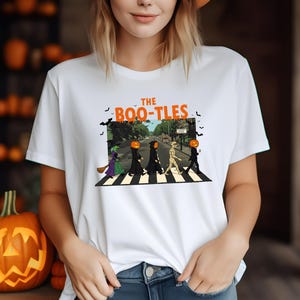 May include: White t-shirt with a Halloween-themed graphic. The design features a parody of the Beatles' Abbey Road album cover, with costumed figures crossing a crosswalk. The text "The Boo-Tles" is above the image.