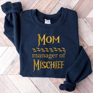 May include: Navy blue sweatshirt with gold lettering that reads "MOM manager of MISCHIEF" with a row of footprints above the word "manager".