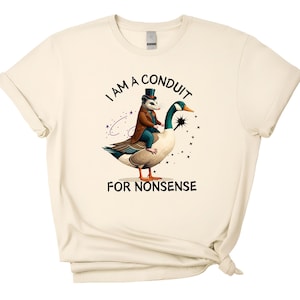 May include: Cream-colored t-shirt featuring a whimsical illustration. An opossum in a top hat and coat rides a goose, with the text "I AM A CONDUIT FOR NONSENSE" above and below the image. The design includes stars.