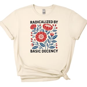 May include: A cream-colored short-sleeve t-shirt featuring a central graphic of red flowers and dark blue leaves. The text RADICALIZED BY BASIC DECENCY is printed in black capital letters above and below the floral illustration on the front.