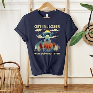 May include: A navy blue t-shirt with a retro-style graphic of a UFO with the text "Get in, loser. We're doing butt stuff."